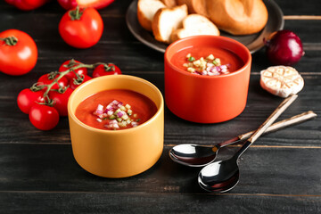 Bowls with tasty gazpacho and vegetables on dark wooden background