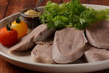 Sliced Beef Tongue Slices on a platter with lettuce leaves, cherry tomatoes and Dijon mustard on a...
