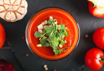 Glass with tasty gazpacho and vegetables on dark background, closeup