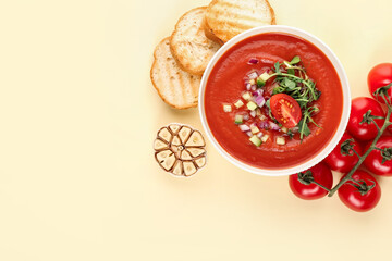 Bowl with tasty gazpacho, garlic, tomato and bread slices on color background