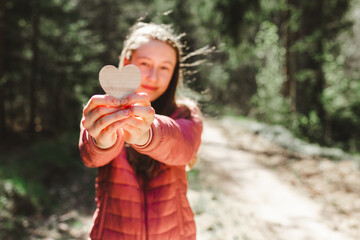 One joyful teen girl in forest holding a wooden heart in her hand.On spring or summer nice day.