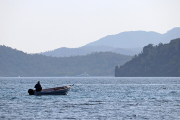 Fishing boat in the sea on background of mountains in mist. Alone fisherman, picturesque seascape