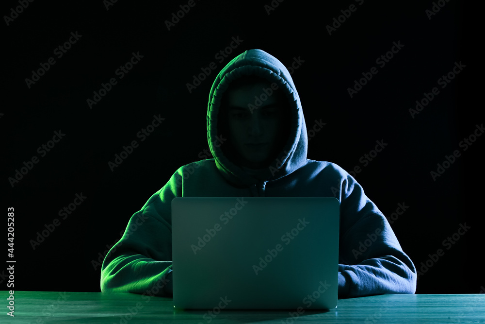 Poster silhouette of hacker with laptop at table on dark background