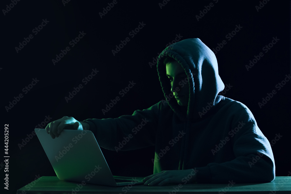 Poster silhouette of hacker with laptop at table on dark background