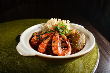 asian premium banquet menu braised seafood combo with big prawn , fish, shell and mushroom in hot clay pot on gold background dining table