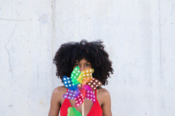 Young and beautiful Afro-American woman holds a windmill in her hands and is spinning it with the air from her lips. Summer concept and colour