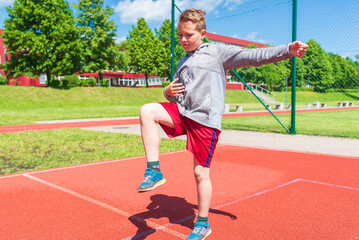 Basketball kid boy player doing stretching at street court.The boy does warm up.Summer street red court sunny day.