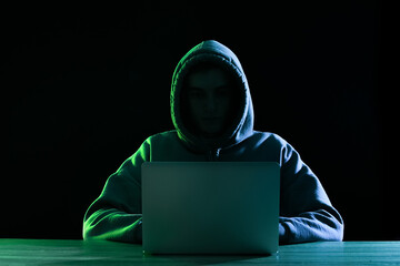 Silhouette of hacker with laptop at table on dark background - obrazy, fototapety, plakaty