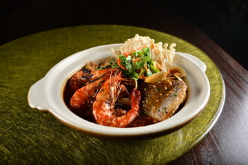 asian premium banquet menu braised seafood combo with big prawn , fish, shell and mushroom in hot clay pot on gold background dining table