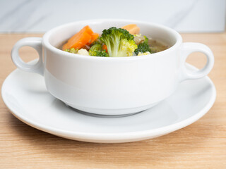 Vegetables soup that contain sausage, broccoli, carrots, etc on a white porcelain bowl