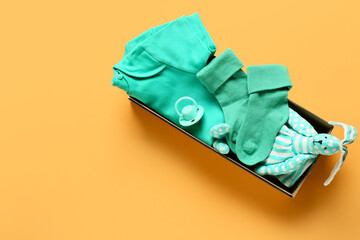 Box with baby clothes, toy and pacifier on color background