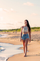 Lonely young woman walking on the beachsunset day.Beach woman in fashion beachwear relaxing walking near summer ocean.