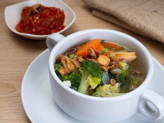 Vegetables soup that contain sausage, broccoli, carrots, etc on a white porcelain bowl