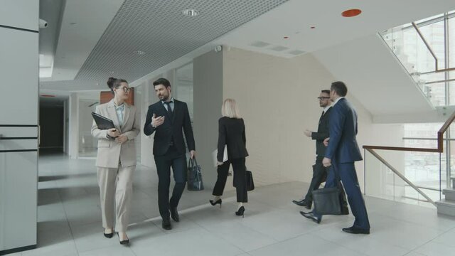 Slowmo shot of male and female lawyers or business people in suits and formalwear talking while walking along modern office working together in law firm