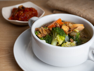 Vegetables soup that contain sausage, broccoli, carrots, etc on a white porcelain bowl