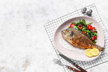 Plate with fried dorado on light background