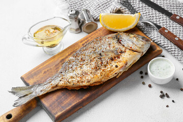 Wooden board with fried dorado on light background