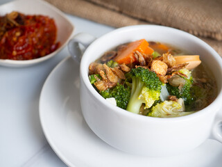 Vegetables soup that contain sausage, broccoli, carrots, etc on a white porcelain bowl