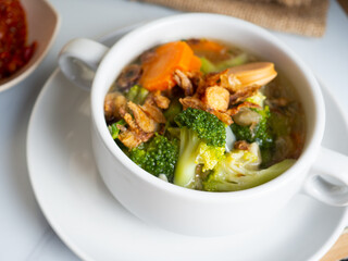 Vegetables soup that contain sausage, broccoli, carrots, etc on a white porcelain bowl