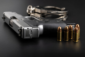 Automatic pistol hand gun with bullets and handcuffs on black background