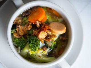 Vegetables soup that contain sausage, broccoli, carrots, etc on a white porcelain bowl