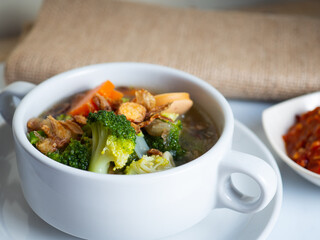 Vegetables soup that contain sausage, broccoli, carrots, etc on a white porcelain bowl