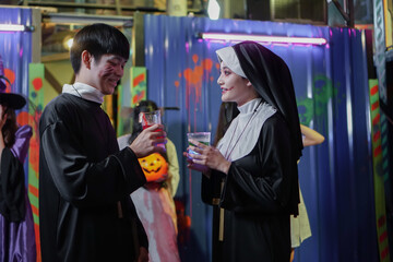 Asian young man and woman dressed as nun and priest make up face for blood and wounds flirt with...