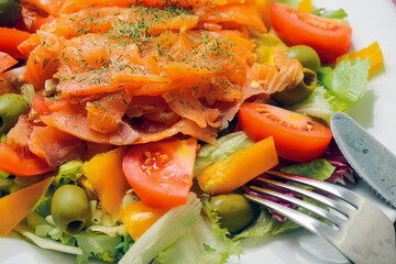 Close up of fresh salad with smoked salmon, tomato, lettuce and green olives and olive oil.