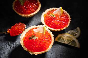 Red caviar in tartlets top view. Red caviar with lemon slices on a black background. Seafood and delicacies.