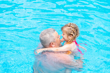 dad and little daughter swim in the pool on summer vacation