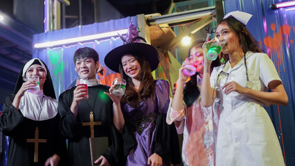 Selective focus on young Asian woman dressed as witch smiling and holding drink at Halloween party...