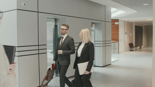 Slowmo shot of male and female lawyers in formalwear working in big law firm together walking through modern office
