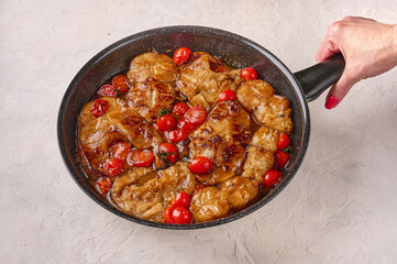 Woman's hand holds frying pan with traditional Sicilian fish with tomatoes and spices on light background, close up