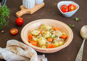 Hearty stew with chicken, barley, carrots and cauliflower in a ceramic bowl on a brown concrete background.