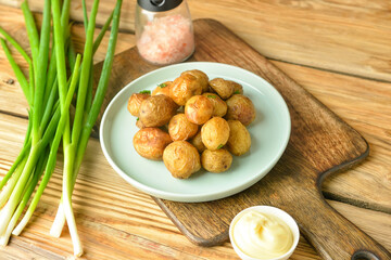 Plate with tasty baked potato and sauce on wooden background