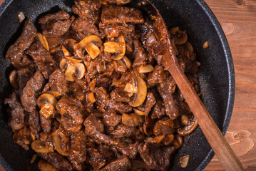 Cooking beef stroganoff - fried pieces of beef and mushrooms in a pan, the second stage of making beef stroganoff