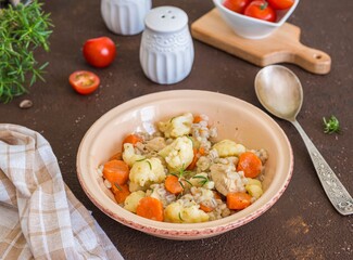 Hearty stew with chicken, barley, carrots and cauliflower in a ceramic bowl on a brown concrete background.