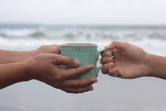 Hands of two people holding a cup of coffee or tea on beach background. Take and give or giving and receive concepts. Kindness concept.