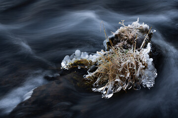 Freezing cold water flowing around a rock with ice and frost at a small river in Iceland
