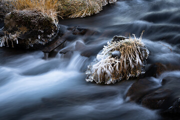 Freezing cold water flowing over rocks with ice and frost at a small river in Iceland