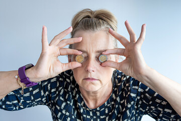 an middle-aged woman holds euro coins in her hands near her eyes