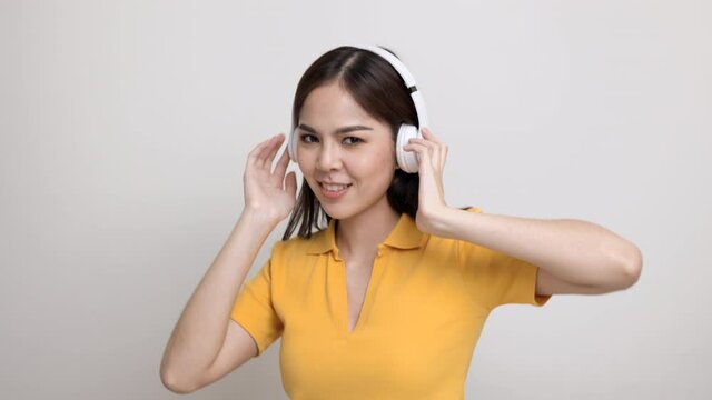 Cute asian female teenager listen to the music with white headphone dancing on isolated. Beautiful young woman in yellow shirt hand touch a wireless headphone having fun with the music in  room.
