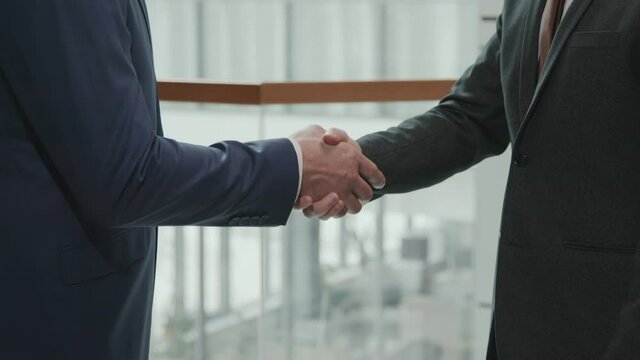 Midsection slowmo of unrecognizable lawyers or business partners in suits shaking hands in office making deal
