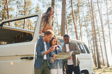 Using map. Group of young people is traveling together in the forest at daytime