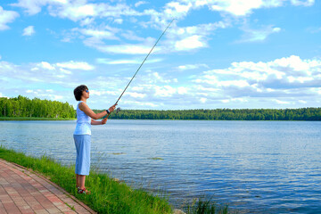 woman fishing on a spinning rod in the lake on summer day, outdoor activities, angler