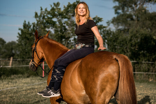 Portrait of young woman sitting sideways on horse. She laughs and enjoys life. Beauty and health life in nature