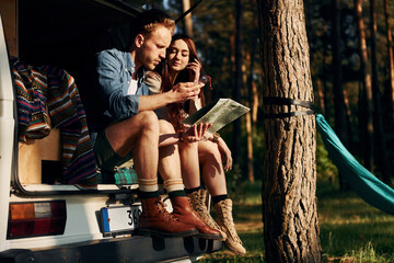 Fototapeta na wymiar Sitting on the back of the car. Young couple is traveling in the forest at daytime together
