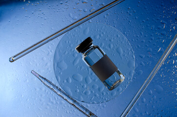 Top view of glass bottle full of medical liquid on the round wet glass, pipettes on the blue surface