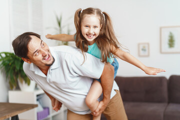 Happy positive cheerful dad is playing with his little charming daughter at home. The man circles and throws the girl up. A dynamic image. Copy space