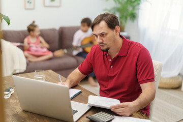 father works at home with a laptop together with the children. small children play the guitar, make noise and interfere with dad's work. a man tries to focus on remote work at home